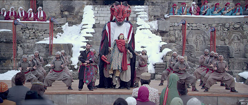 Screenshot of one life-size puppet being attacked by a much larger puppet, both being operated by dancers on stage